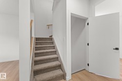 Hardwood-style flooring, carpeted staircase, light wood handrail, and white panel door with black hardware - 