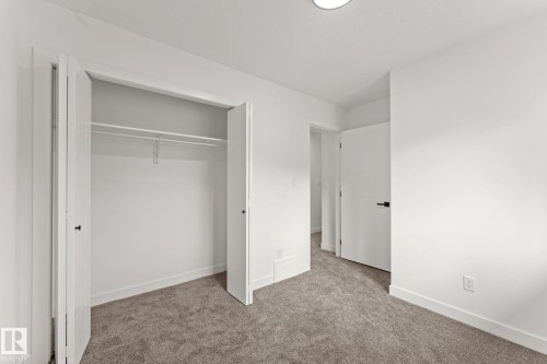 White walls with broad baseboards, textured carpeting, closet with bi-fold doors, and a flush mount ceiling light - 10825 93 Street Nw, Edmonton, AB - Indoor Photo Showing Other Room