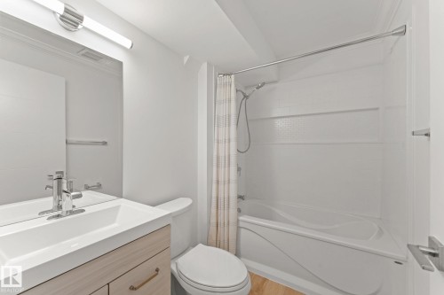 Bathroom with a built-in bathtub and shower combination, chrome fixtures, a wood-finish vanity with an integrated sink, and an overhead vanity light - 10825 93 Street Nw, Edmonton, AB - Indoor Photo Showing Bathroom