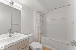 Bathroom with a built-in bathtub and shower combination, chrome fixtures, a wood-finish vanity with an integrated sink, and an overhead vanity light - 