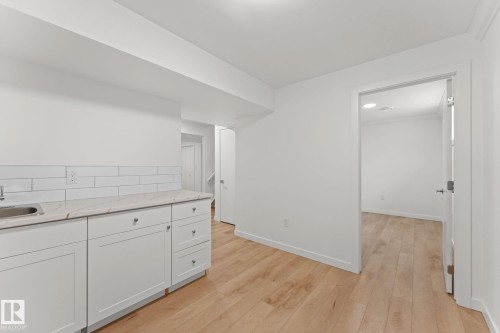 White cabinetry with metal hardware, light-toned wood-finish flooring, undermount sink, marble-look countertop, and white subway tile backsplash - 10825 93 Street Nw, Edmonton, AB - Indoor Photo Showing Other Room