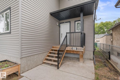 Exterior featuring light grey siding, a covered porch with dark trim, wood steps, and black metal railings - 10825 93 Street Nw, Edmonton, AB - Outdoor With Exterior