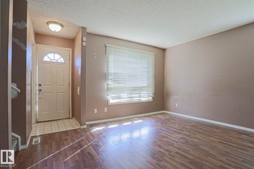 Wood-finish flooring throughout, featuring a front entry door with a decorative transom, a window with horizontal blinds, and a flush-mount ceiling light fixture - #45 1651 46 St Nw, Edmonton, AB - Indoor Photo Showing Other Room