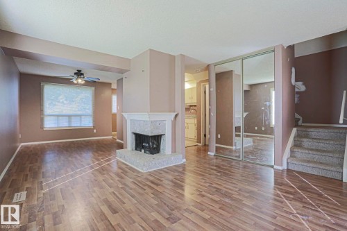 Wood-finish flooring throughout, featuring a corner fireplace with a tiled surround, a ceiling fan with integrated lighting, and mirrored closet doors - #45 1651 46 St Nw, Edmonton, AB - Indoor With Fireplace