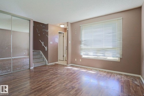 Wood-finish flooring, staircase with carpeted treads, mirrored closet doors, and window with blinds - #45 1651 46 St Nw, Edmonton, AB - Indoor Photo Showing Other Room