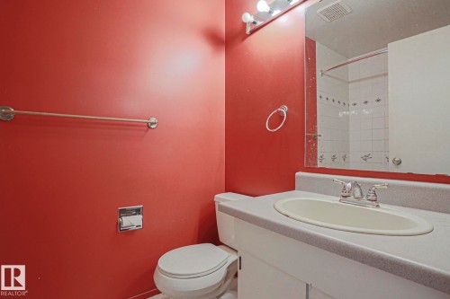 White porcelain commode, integrated vanity sink, chrome faucet, wall-mounted mirror, and white tile shower surround - #45 1651 46 St Nw, Edmonton, AB - Indoor Photo Showing Bathroom