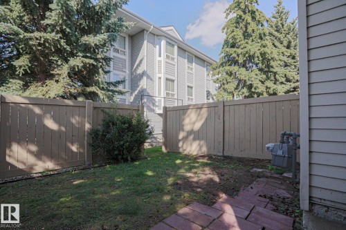 Fenced yard featuring a grass area, brick paver section, and mature evergreen trees - #45 1651 46 St Nw, Edmonton, AB - Outdoor