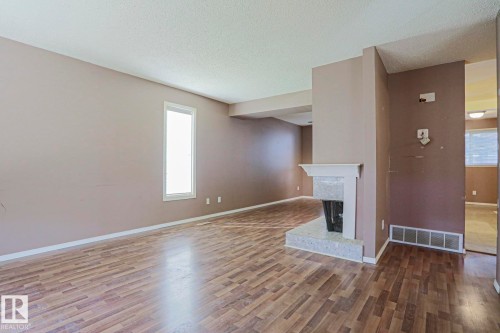 Spacious interior with wood-finish flooring, neutral wall tones, a single vertical window, and a built-in fireplace with a light-toned surround - #45 1651 46 St Nw, Edmonton, AB - Indoor Photo Showing Other Room