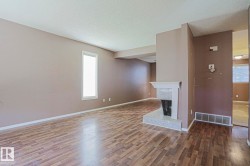 Spacious interior with wood-finish flooring, neutral wall tones, a single vertical window, and a built-in fireplace with a light-toned surround - 