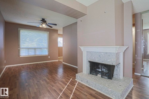 Wood-finish flooring throughout, featuring a fireplace with a light-toned stone surround and hearth, a white mantel, and a ceiling fan - #45 1651 46 St Nw, Edmonton, AB - Indoor Photo Showing Living Room With Fireplace
