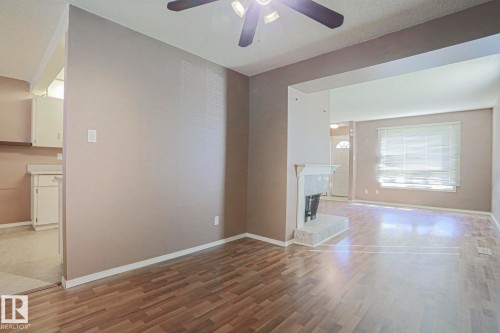 Wood-finish flooring, ceiling fan, white kitchen cabinetry, white kitchen countertops, and fireplace with a light-toned hearth - #45 1651 46 St Nw, Edmonton, AB - Indoor Photo Showing Other Room