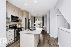 Kitchen featuring light wood-finish cabinetry, stainless steel appliances, a center island with sink, and wood-finish flooring - 
