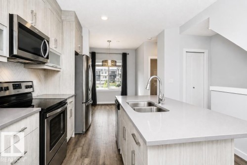 Contemporary kitchen featuring stainless steel appliances, a center island with a double basin sink, light-toned cabinetry, and wood-finish flooring - #6 215 Saddleback Rd Nw, Edmonton, AB - Indoor Photo Showing Kitchen With Double Sink With Upgraded Kitchen