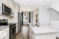 Contemporary kitchen featuring stainless steel appliances, a center island with a double basin sink, light-toned cabinetry, and wood-finish flooring - 