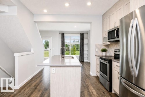 Open-concept kitchen with stainless steel appliances, wood-finish flooring, light-toned cabinetry, and an island with an undermount sink - #6 215 Saddleback Rd Nw, Edmonton, AB - Indoor Photo Showing Kitchen