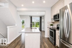 Open-concept kitchen with stainless steel appliances, wood-finish flooring, light-toned cabinetry, and an island with an undermount sink - 