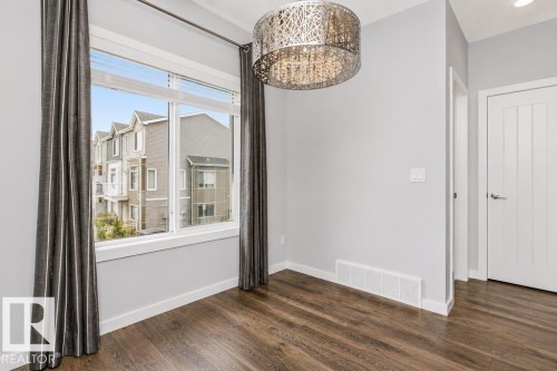 Wood-finish flooring, a large window, a decorative chandelier, white trim, and a white interior door - #6 215 Saddleback Rd Nw, Edmonton, AB - Indoor Photo Showing Other Room
