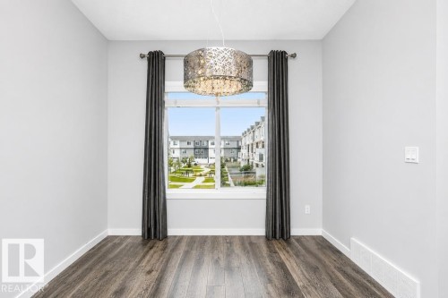 Bright window with white trim, wood-finish flooring, and a modern chandelier - #6 215 Saddleback Rd Nw, Edmonton, AB - Indoor Photo Showing Other Room