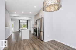 Wood-finish flooring throughout, kitchen island with built-in sink, stainless steel appliances, recessed lighting, and a decorative pendant light fixture - 