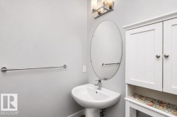 Pedestal sink with chrome faucet, oval mirror, wall-mounted light fixture, white storage cabinet with beadboard doors, and chrome towel bar - 