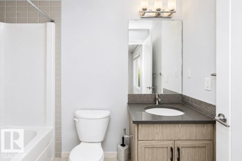 Bathroom featuring a built-in tub and shower combination, vanity with dark countertop, integrated sink, and modern vanity lighting - #6 215 Saddleback Rd Nw, Edmonton, AB - Indoor Photo Showing Bathroom
