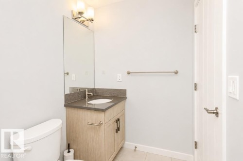 Vanity with integrated sink, stone countertop, wood-finish cabinetry, and brushed nickel hardware - #6 215 Saddleback Rd Nw, Edmonton, AB - Indoor Photo Showing Bathroom