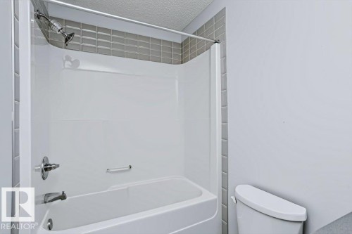 Tub/shower combination with a white surround, gray tile accent, and polished chrome fixtures - #6 215 Saddleback Rd Nw, Edmonton, AB - Indoor Photo Showing Bathroom