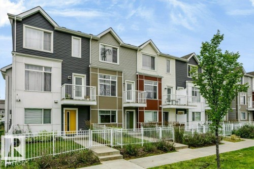 Contemporary townhome exterior with varied siding textures, private balconies, individual entrances, white picket fencing, and concrete walkways - #6 215 Saddleback Rd Nw, Edmonton, AB - Outdoor With Facade