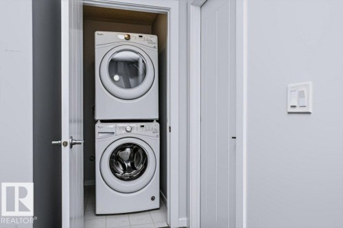 Dedicated laundry closet featuring stacked front-load washer and dryer units with white finish - #6 215 Saddleback Rd Nw, Edmonton, AB - Indoor Photo Showing Laundry Room
