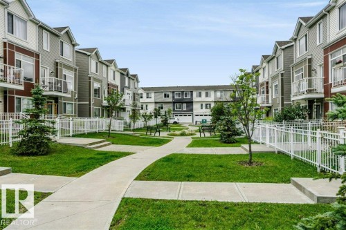 Manicured green spaces with concrete pathways, multi-story residences featuring balconies, and white fencing - #6 215 Saddleback Rd Nw, Edmonton, AB - Outdoor With Facade