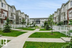 Manicured green spaces with concrete pathways, multi-story residences featuring balconies, and white fencing - 