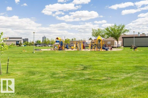 Expansive green space featuring a large playground area with multiple structures, surrounded by mature trees and paved paths - #6 215 Saddleback Rd Nw, Edmonton, AB - Outdoor