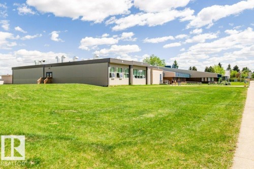 Expansive green lawn, multi-level building structure, multiple windows, flat roof, and a paved walkway - #6 215 Saddleback Rd Nw, Edmonton, AB - Outdoor