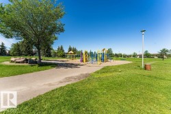 Expansive green space featuring a paved pathway, mature trees, and a dedicated play area - 
