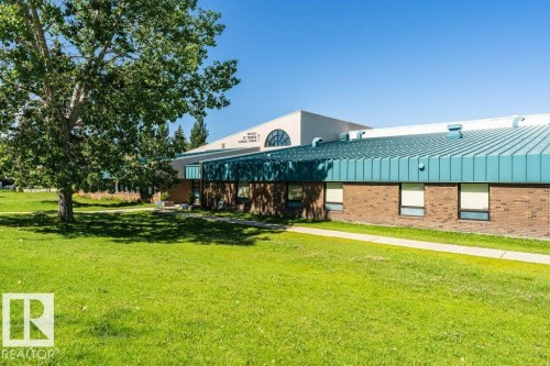 Expansive green space with mature trees, a brick facade building, and a teal metal roof - #6 215 Saddleback Rd Nw, Edmonton, AB - Outdoor