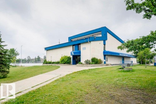 Building exterior with blue architectural accents and light-colored siding, featuring a paved walkway - #6 215 Saddleback Rd Nw, Edmonton, AB - Outdoor