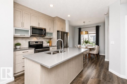 Kitchen featuring light wood-finish cabinetry, stainless steel appliances, a center island with an undermount sink, and wood-finish flooring - #6 215 Saddleback Rd Nw, Edmonton, AB - Indoor Photo Showing Kitchen With Double Sink With Upgraded Kitchen