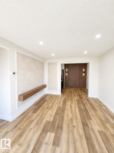 Wood-finish flooring throughout, recessed ceiling lighting, textured wall paneling with a floating wood shelf, and an archway leading to an area with wood paneling and sconce lighting - 224 Callingwood Two Two Nw, Edmonton, AB - Indoor Photo Showing Other Room