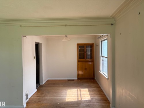 Bright, open room featuring hardwood flooring, abundant natural light from dual windows, and original wood-finish cabinetry with glass-front doors - 10845 140 Street Nw, Edmonton, AB - Indoor Photo Showing Other Room