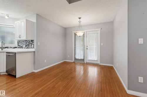 Hardwood flooring throughout, white cabinetry with contemporary pulls, mosaic tile backsplash, stainless steel dishwasher, and a multi-light pendant fixture - #8 1920 Millwoods Rd E Nw, Edmonton, AB - Indoor Photo Showing Other Room