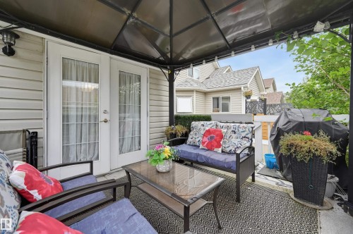 Covered outdoor patio with a patterned area rug, double french doors, and privacy fencing - #8 1920 Millwoods Rd E Nw, Edmonton, AB - Outdoor With Deck Patio Veranda With Exterior