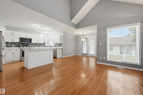 Open-concept living and dining area featuring rich wood-finish flooring, vaulted ceilings with exposed beams, and abundant natural light from expansive glass sliding doors - #8 1920 Millwoods Rd E Nw, Edmonton, AB - Indoor Photo Showing Kitchen With Upgraded Kitchen