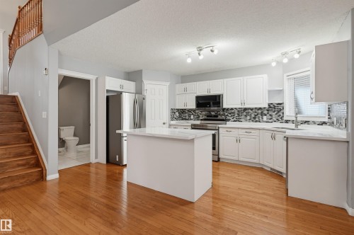 Kitchen featuring white shaker-style cabinetry, a central island, stainless steel appliances, mosaic tile backsplash, and light-toned countertops - #8 1920 Millwoods Rd E Nw, Edmonton, AB - Indoor Photo Showing Kitchen With Upgraded Kitchen