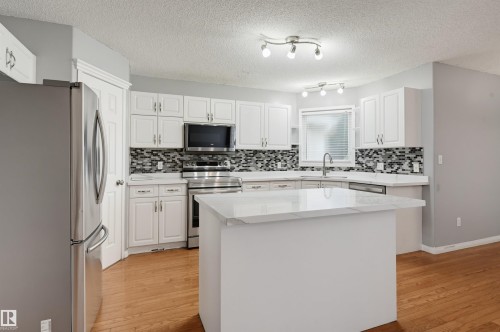 Kitchen with white cabinetry, light countertops, mosaic tile backsplash, and wood-finish flooring - #8 1920 Millwoods Rd E Nw, Edmonton, AB - Indoor Photo Showing Kitchen With Upgraded Kitchen