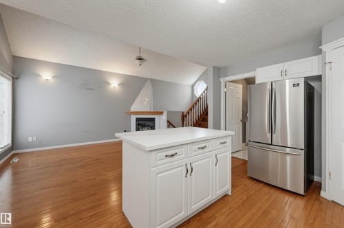 Open-concept living area with wood-finish flooring, a white kitchen island, and stainless steel refrigerator - #8 1920 Millwoods Rd E Nw, Edmonton, AB - Indoor Photo Showing Kitchen