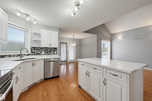 Kitchen featuring white cabinetry, stainless steel appliances, a mosaic tile backsplash, and a central island with a solid surface countertop - #8 1920 Millwoods Rd E Nw, Edmonton, AB - Indoor Photo Showing Kitchen With Double Sink With Upgraded Kitchen