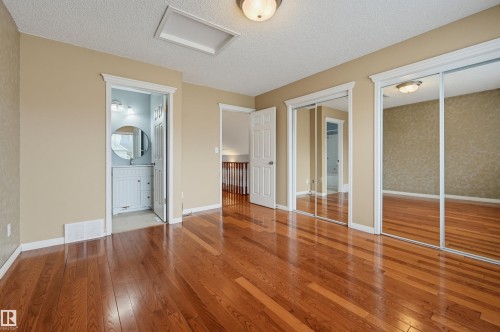 Hardwood flooring, mirrored closet doors, a built-in vanity with a circular mirror, and white trim - #8 1920 Millwoods Rd E Nw, Edmonton, AB - Indoor Photo Showing Other Room