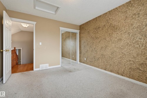 Carpeted room with a textured accent wall, mirrored closet doors, and a ceiling light fixture - #8 1920 Millwoods Rd E Nw, Edmonton, AB - Indoor Photo Showing Other Room