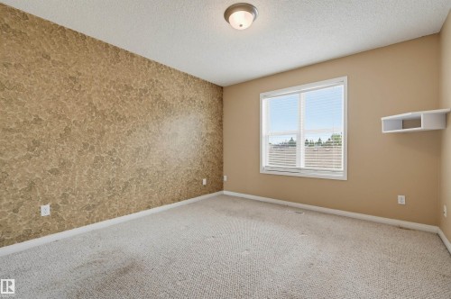 Textured accent wall, neutral wall paint, single window with blinds, overhead flush mount light, and built-in shelving - #8 1920 Millwoods Rd E Nw, Edmonton, AB - Indoor Photo Showing Other Room