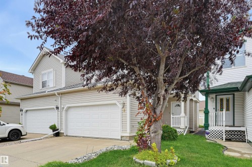 Two-car garage with white paneled doors, light grey horizontal siding, and a white front entry door with side windows - #8 1920 Millwoods Rd E Nw, Edmonton, AB - Outdoor